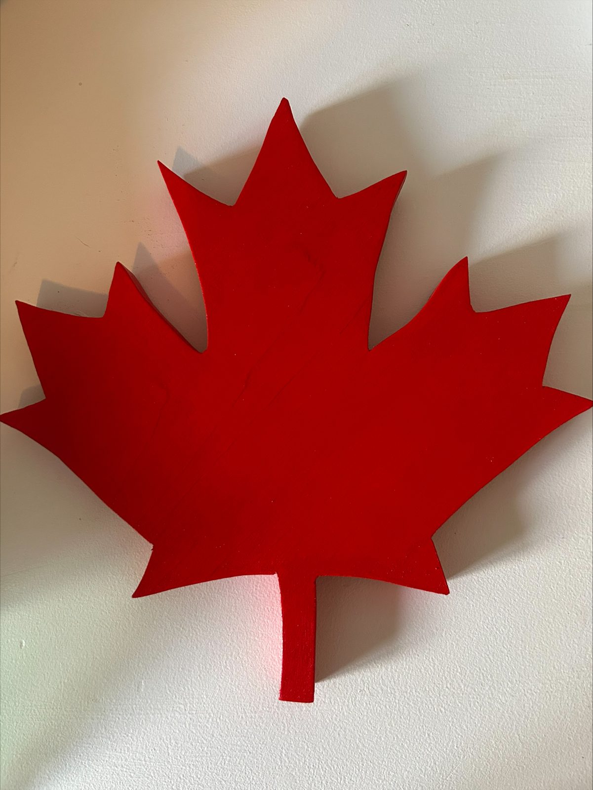 Finished wooden maple leaf painted solid Canadian red, hanging on a white wall
