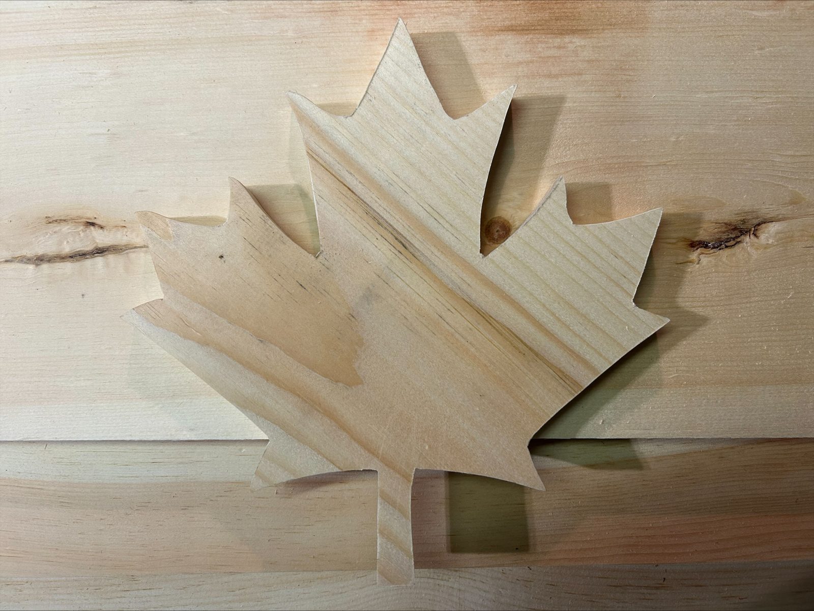 Freshly hand-cut maple leaf in unfinished Canadian pine lying on pine boards