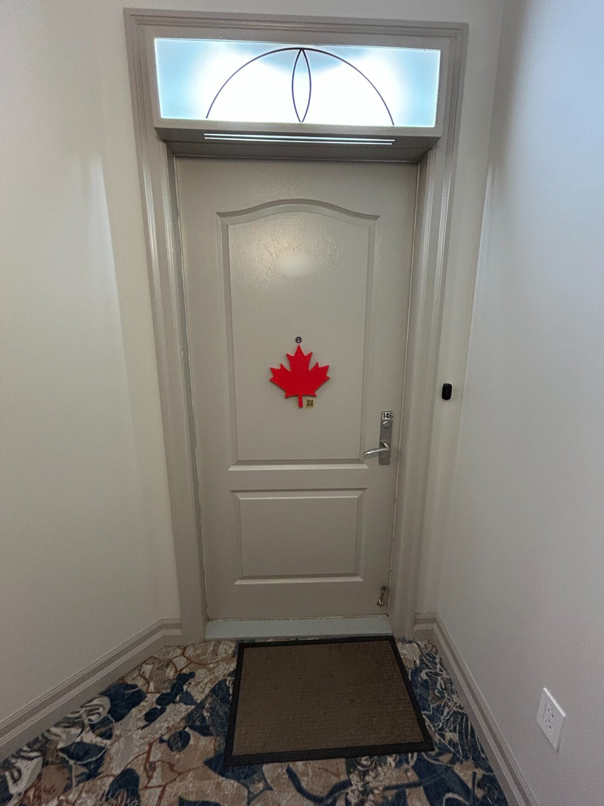 Solid-red wooden maple leaf mounted on a beige apartment door in a senior residence hallway