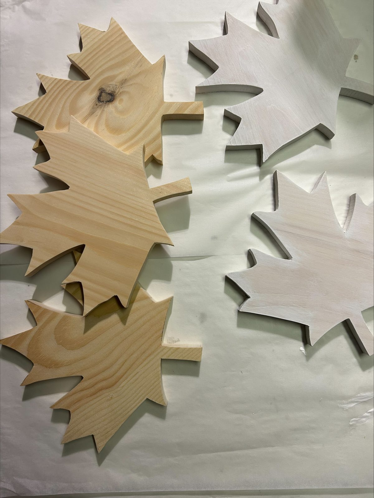 Hand-cut pine maple leaves on a workbench, three natural and two primed white before painting